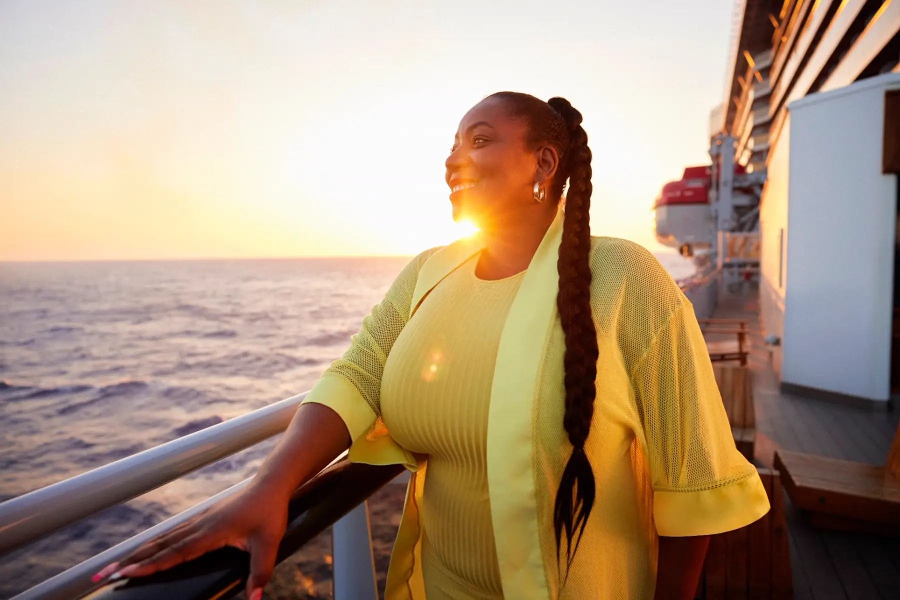 A woman standing at the ship's rail at sunset, looking out over the open ocean