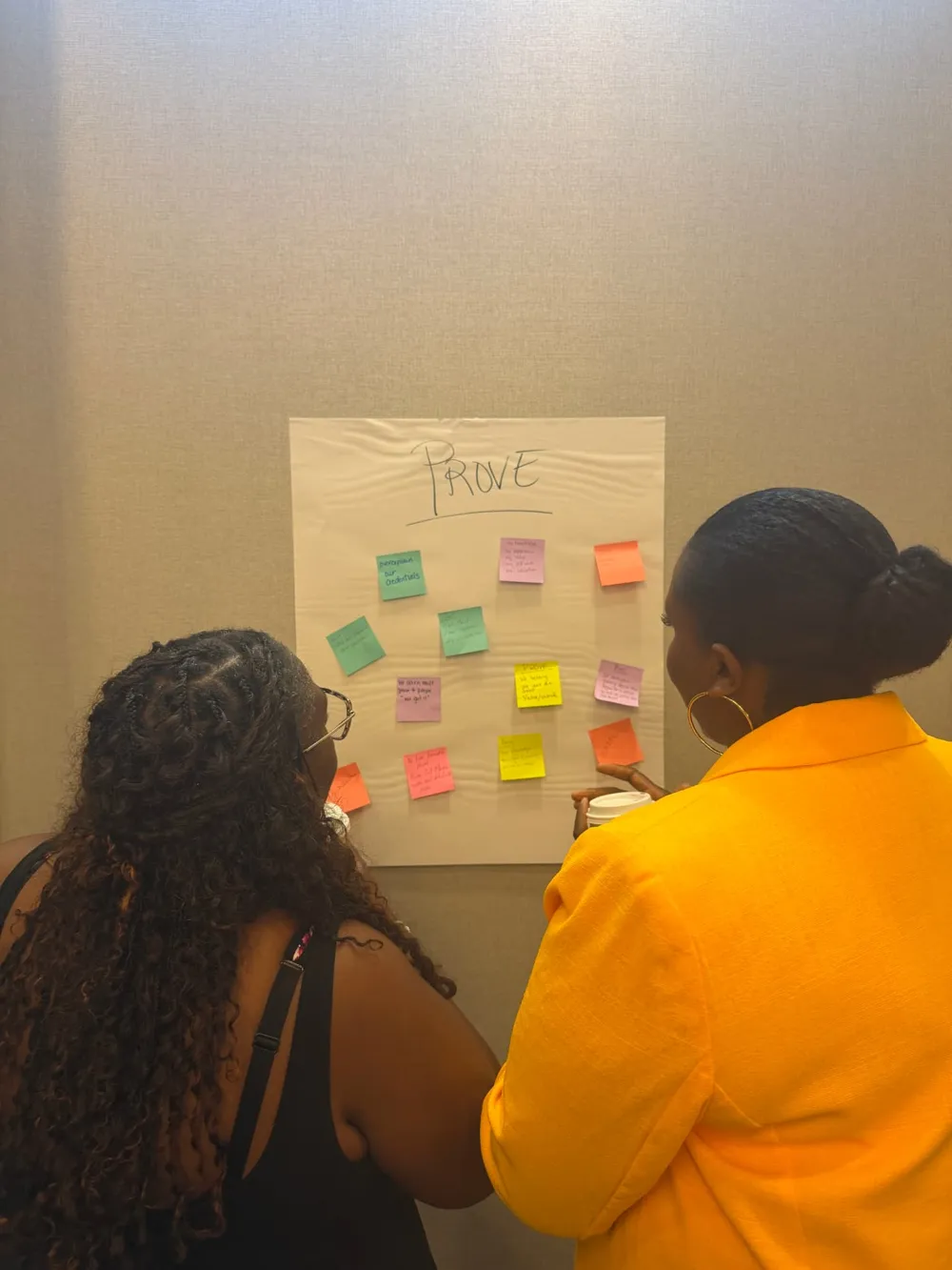 Two women reading sticky-note reflections on a poster titled “PROVE”